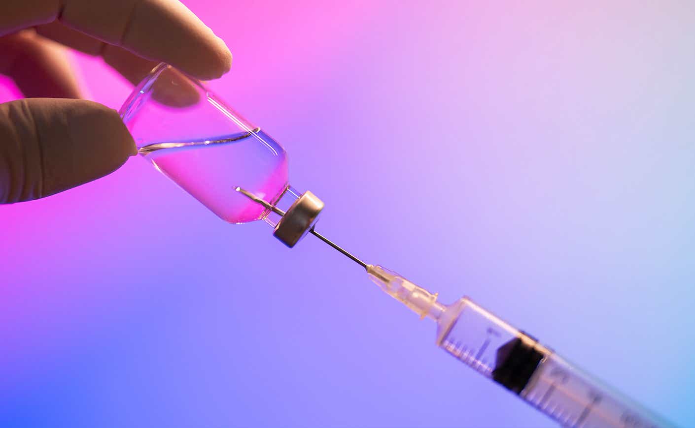 Person holding a syringe against a pink/purple background