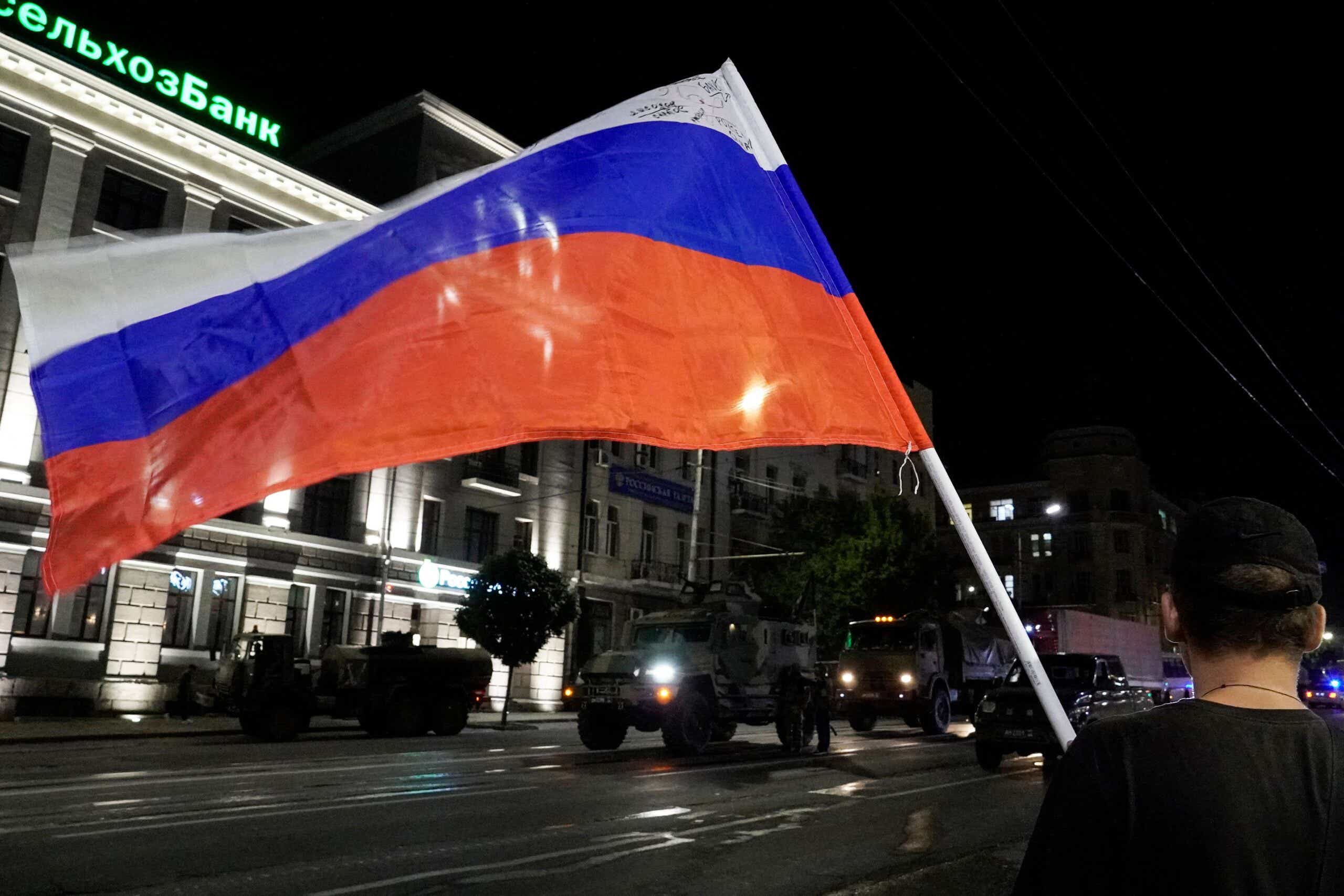 A man waves the Russian national flag as the members of Wagner group prepare to pull out from the headquarters of the Southern Military District