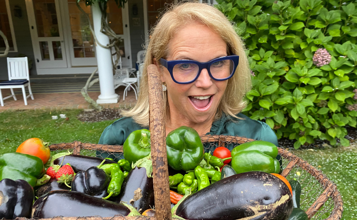 Katie Couric holding up eggplant, peppers, and other veggies in a basket