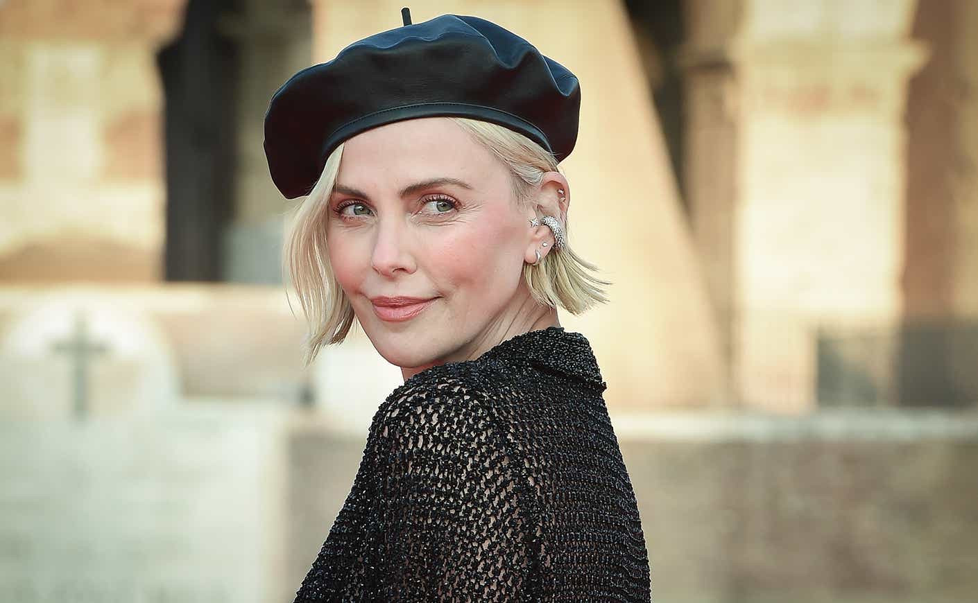 Charlize Theron wears a beret and looks over her shoulder, smiling