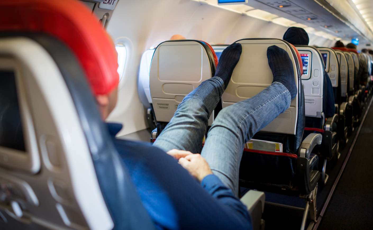 A man putting his feet on a plane headrest, with no shoes on