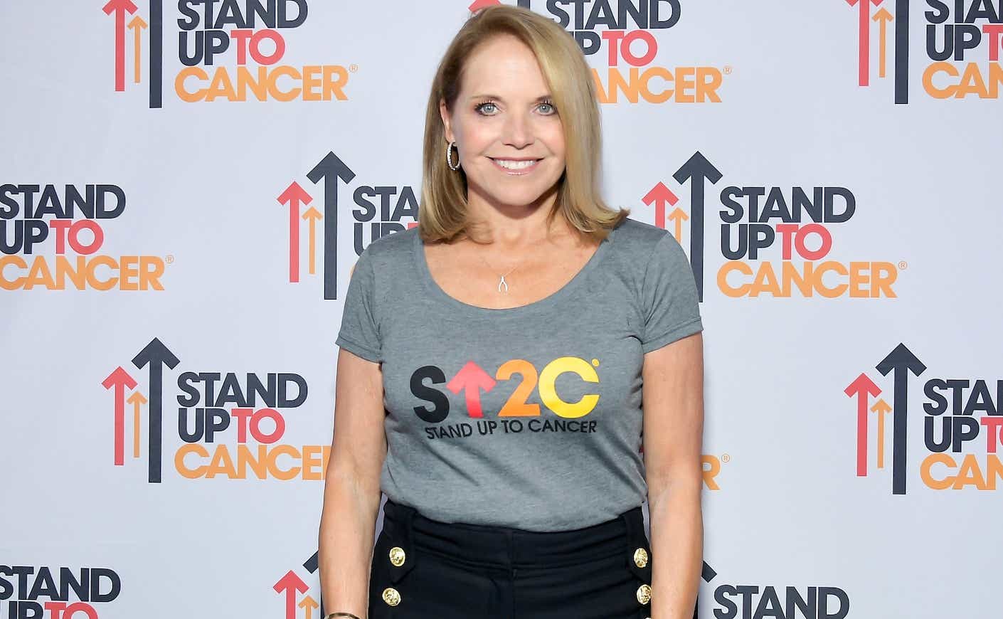katie couric in front of a stand up to cancer step and repeat