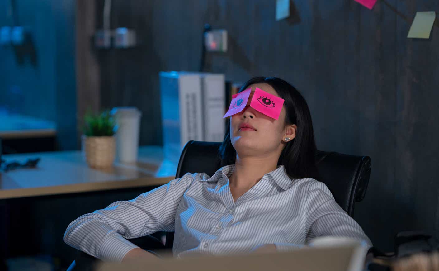 a woman with drawn on eyes sleeps at her desk