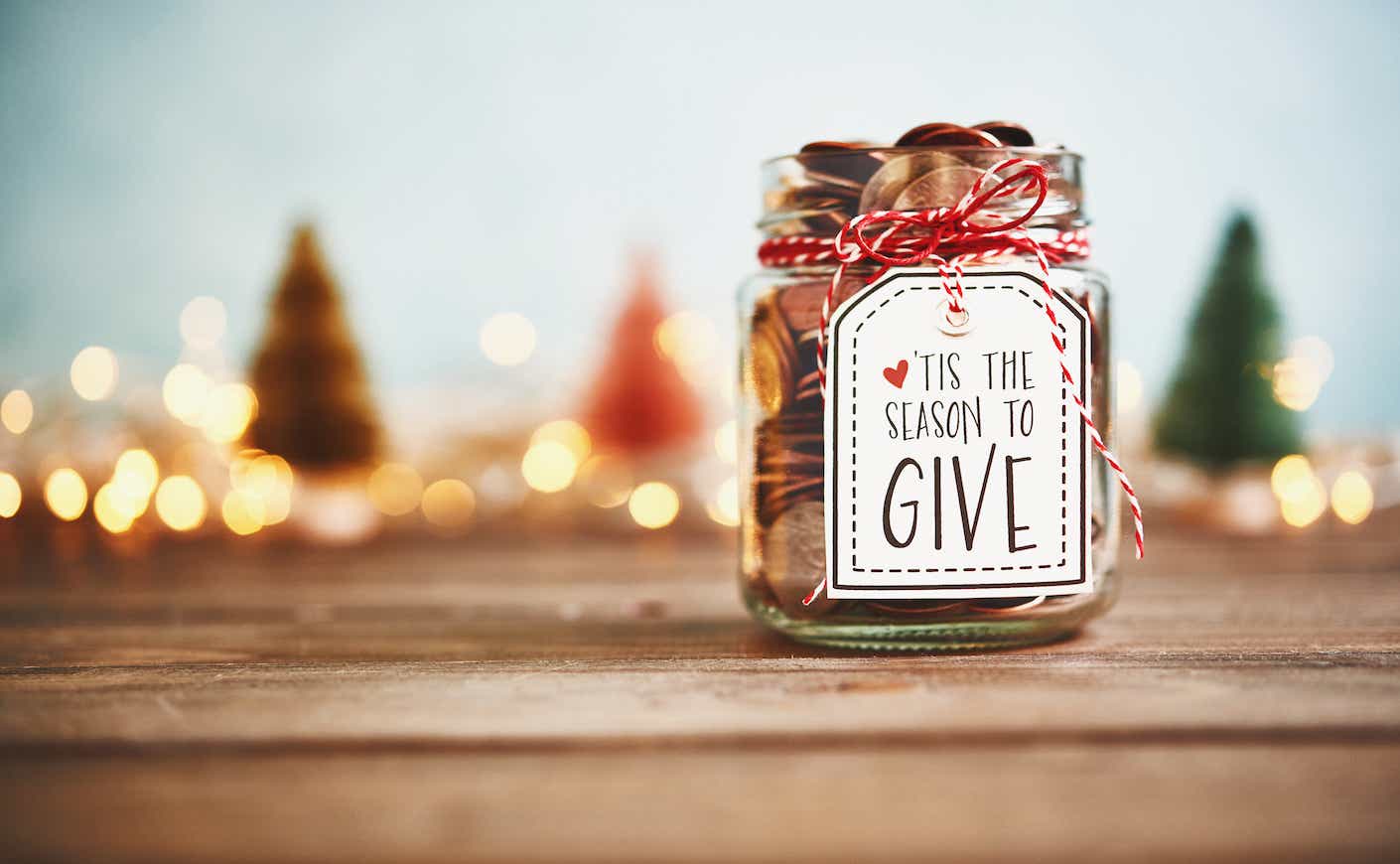 Donation jar with money and a sign that says "tis the season for giving"