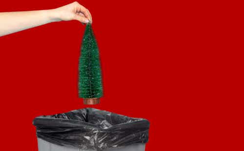 woman holding a small fake christmas tree over the garbage
