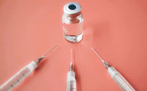 three needles pointing toward a vial of vaccine