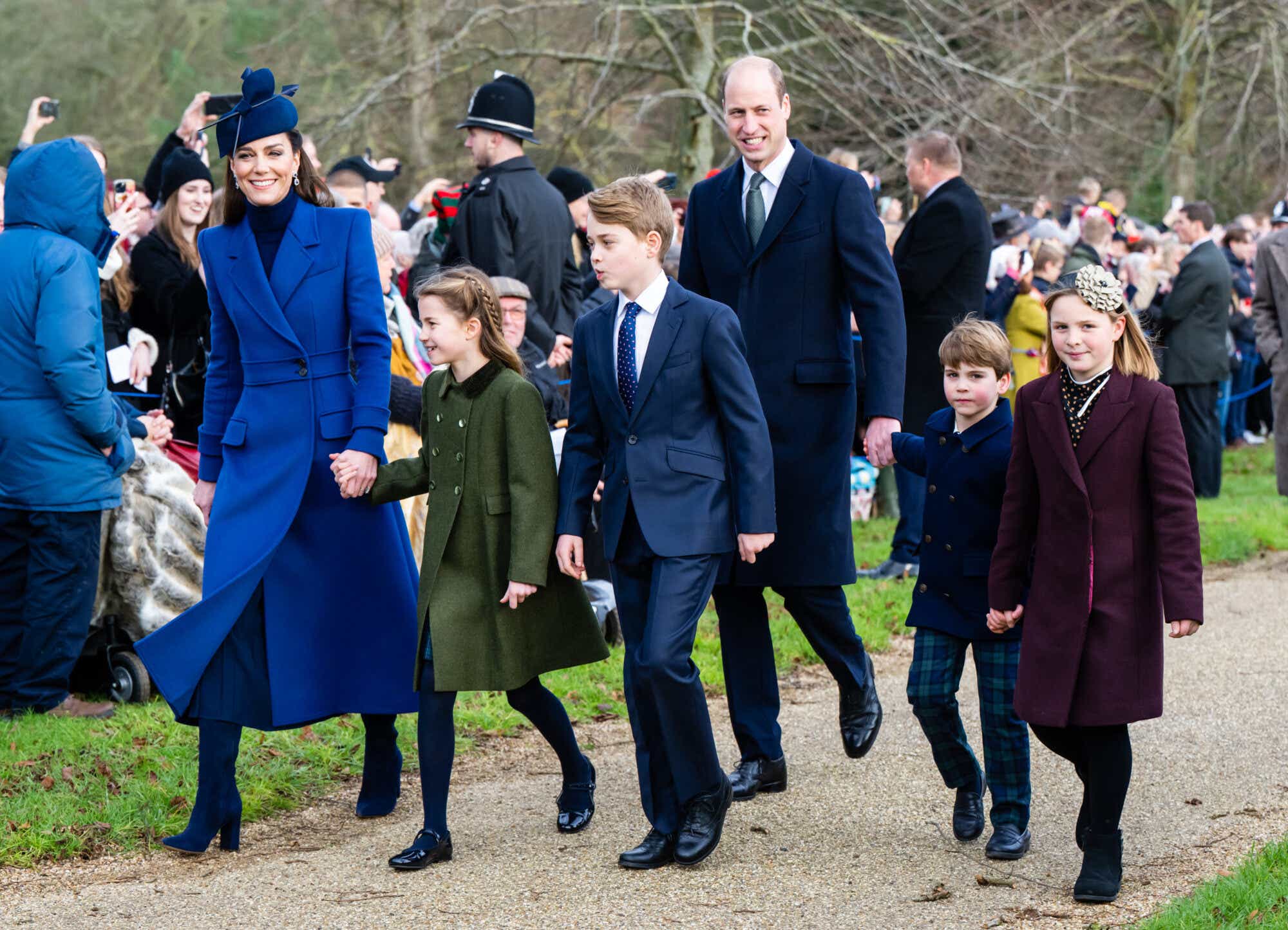 Kate Middleton and her children with Prince William on Christmas Day, 2023. Kate is wearing a long royal blue coat and matching fascinator; Charlotte is in an olive green coat. Prince William and the boys are wearing navy.