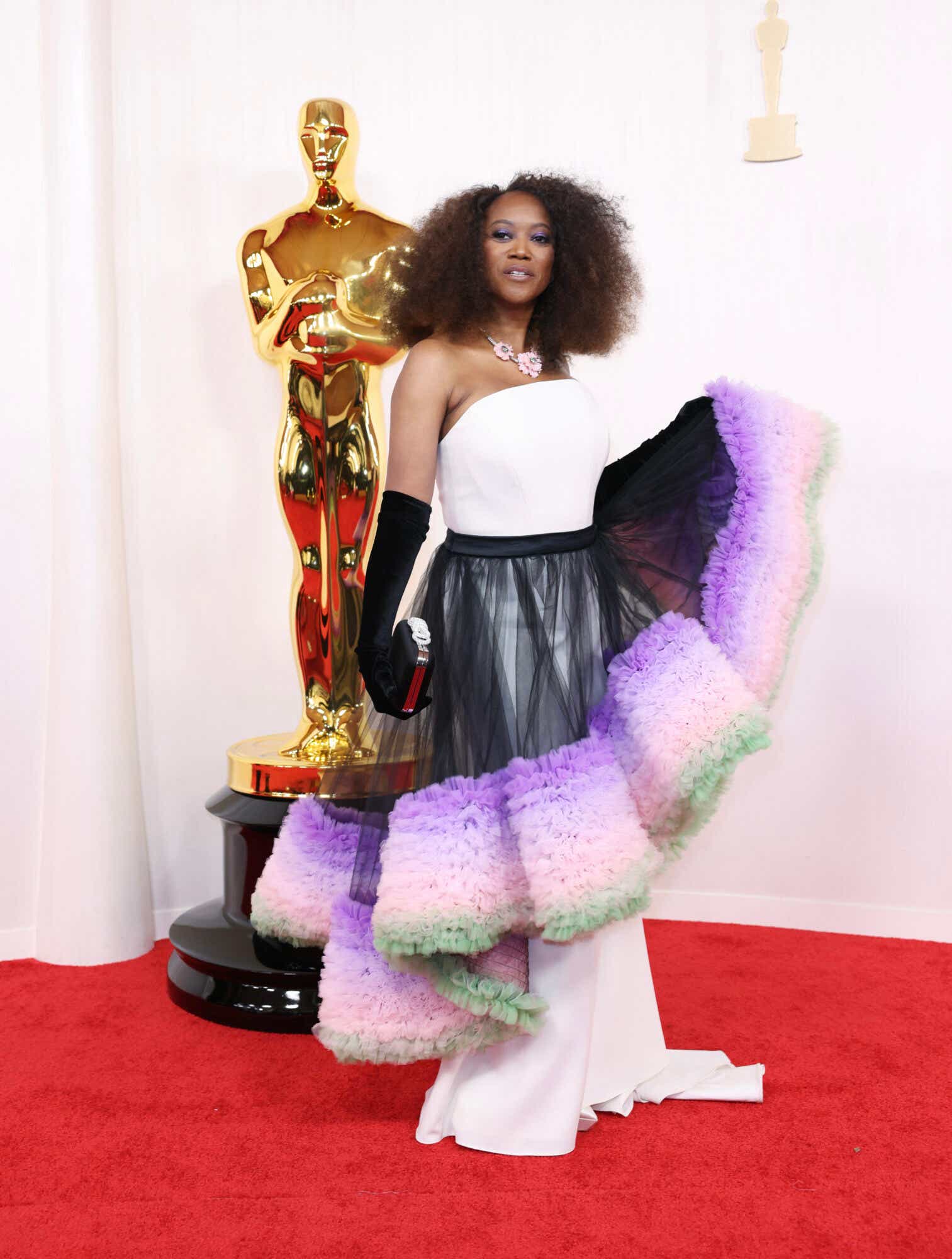 Erika Alexander arrives at the Oscars wearing a white gown with a black tulle skirt overlay. The skirt has purple, pink, and green ruffles. She's also sporting black gloves.