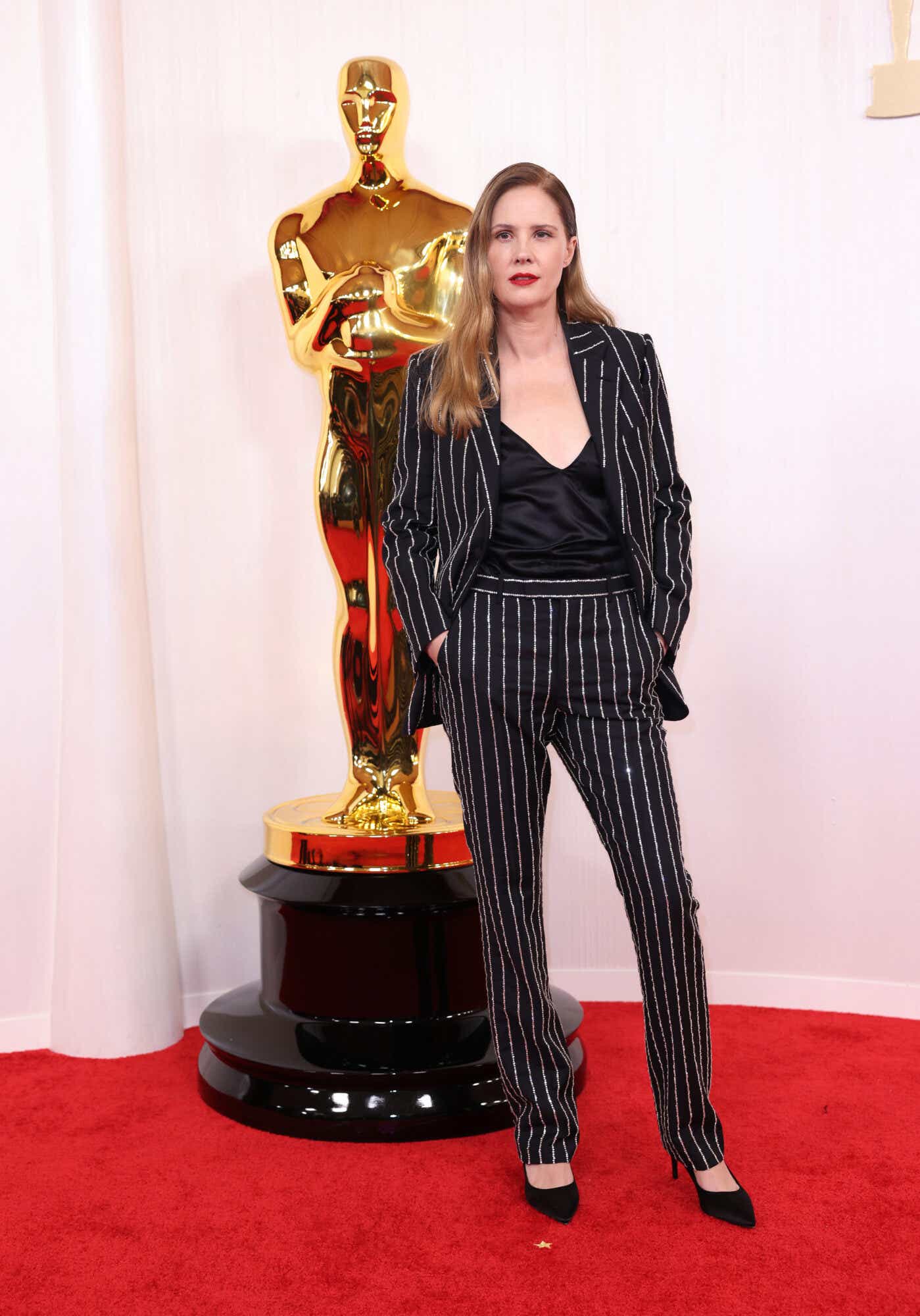 Justine Triet wears a black suit bejeweled in a pinstripe pattern to the Oscars and a black silky top.