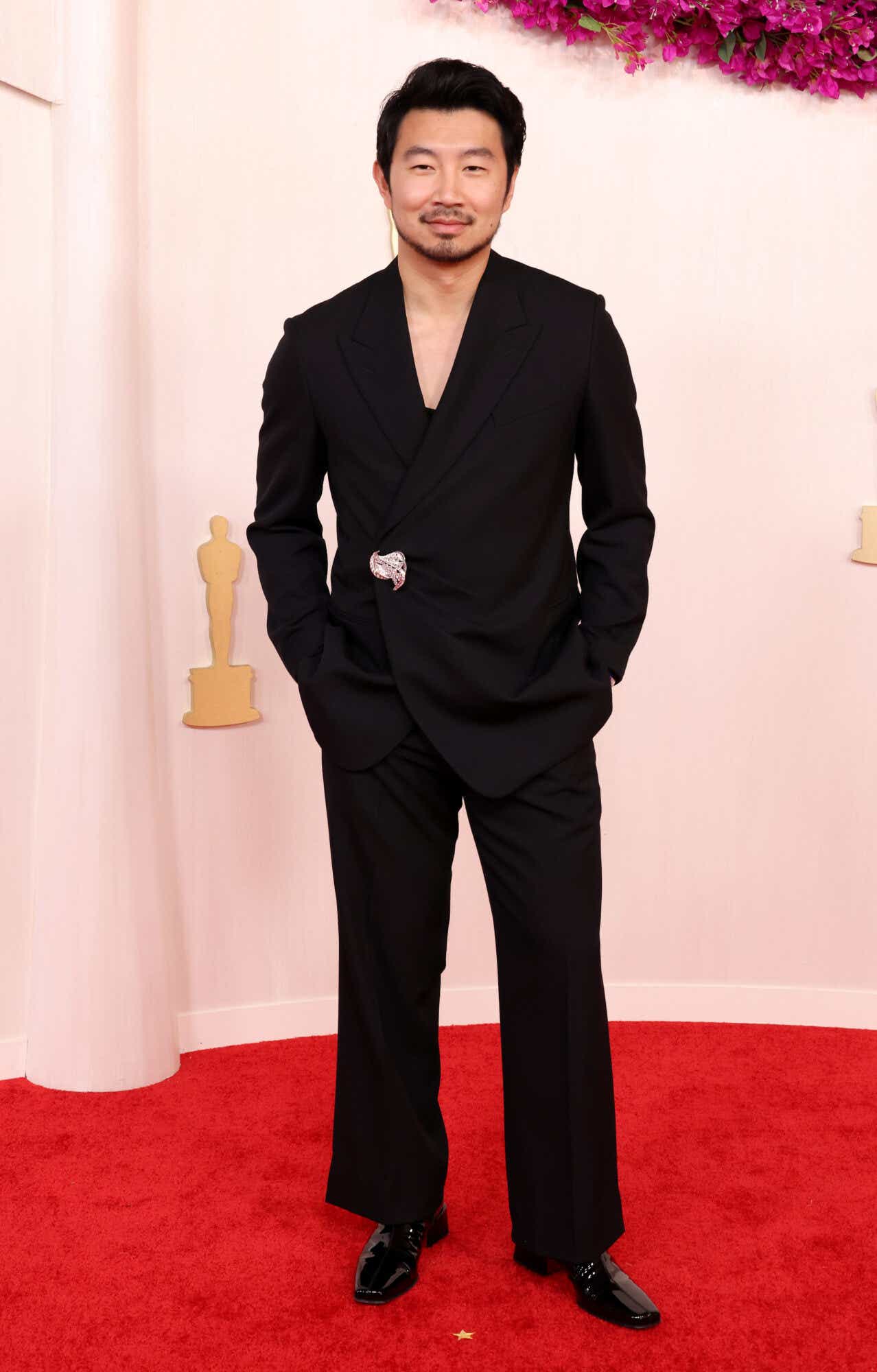 Simu Liu wears an all-black suit and shirt to the Oscars with a brooch.