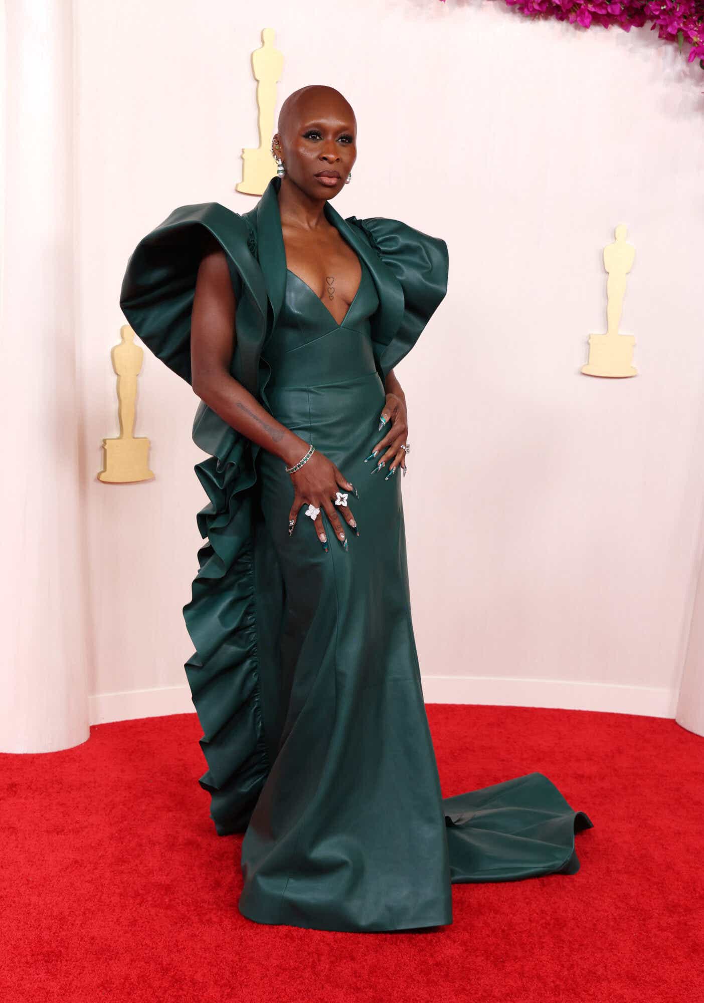 Cynthia Erivo arrives at the Oscars wearing a teal gown with dramatic shoulders and a ruffle down the side. Her long nails match her gown.
