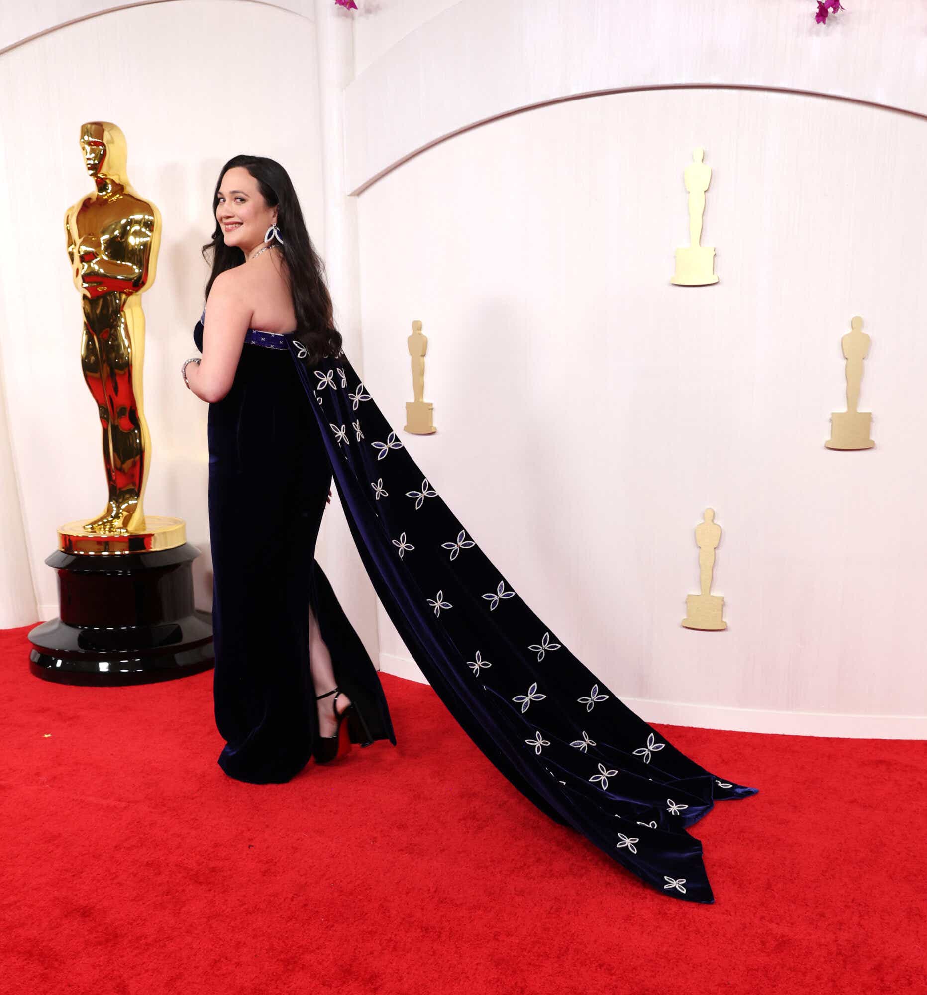 Lily Gladstone wears a navy gown with a long cape to the Oscars.