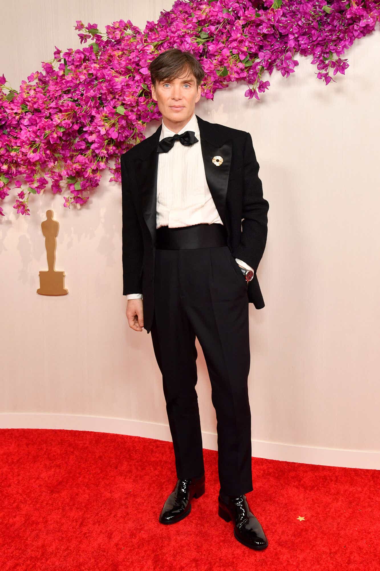 Cillian Murphy wears a black tuxedo with a black bowtie to the Oscars. On his lapel is a gold circular pin. 