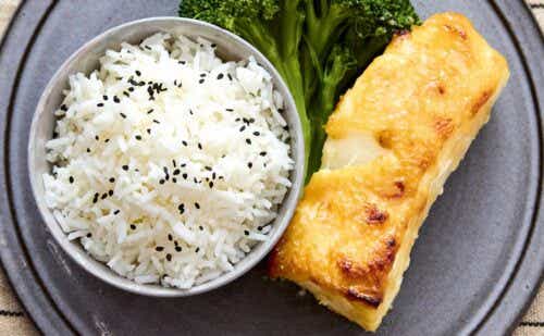 A piece of cod alongside a bowl of rice and piece of broccoli.