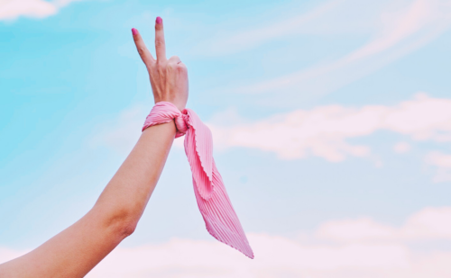 a woman holding up a piece sign with her fingers and a pink scarf on her wrist