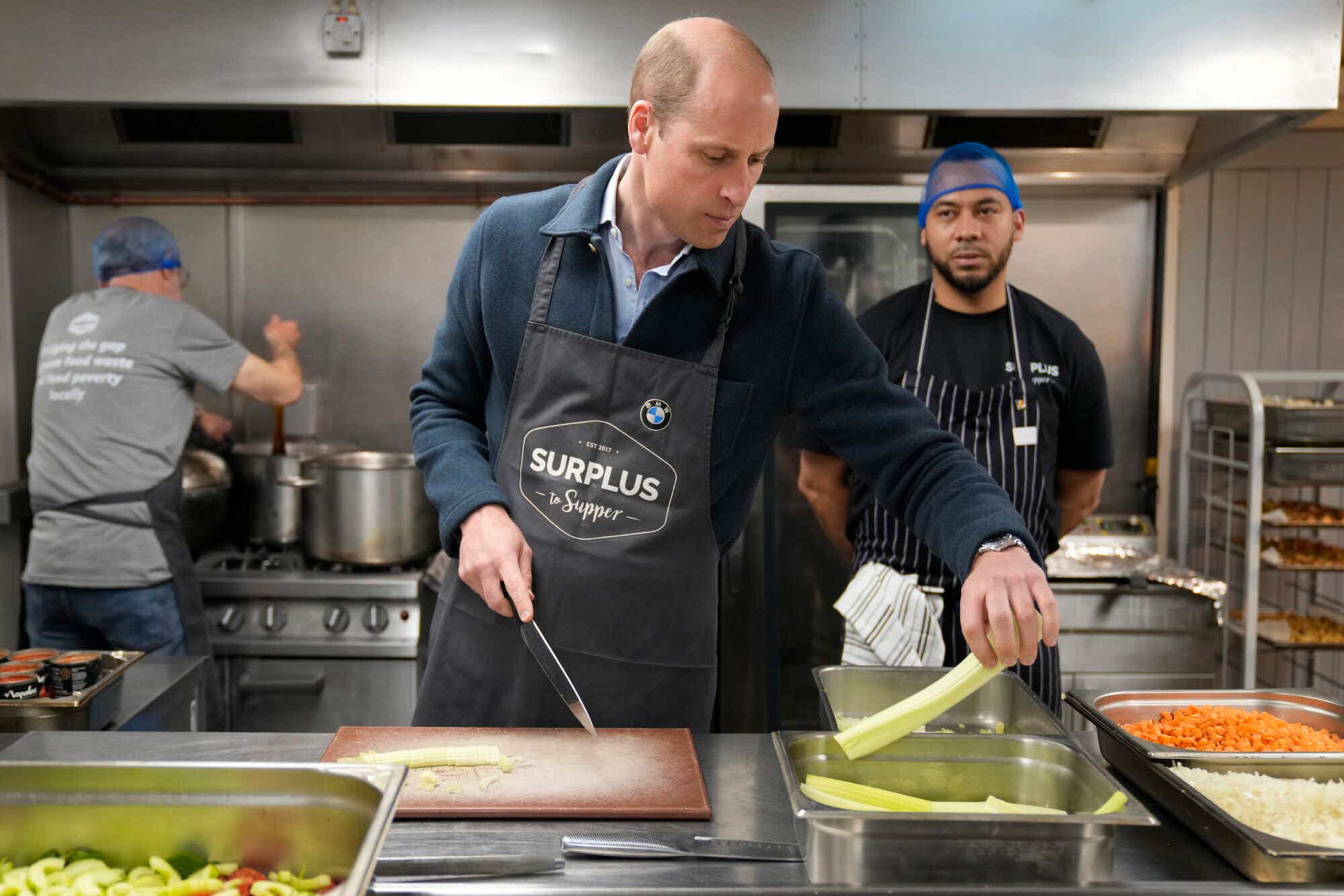 SUNBURY, ENGLAND - APRIL 18: Prince William, Prince of Wales speaks with head chef Mario Confait, (R) as he cuts celery while helping to make a bolognese sauce during a visit to Surplus to Supper, in Sunbury-on-Thames on April 18, 2024 in Surrey, England. 