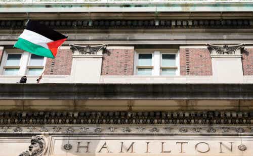 Masked person waves Palestinian flag on top of Columbia's Hamilton Hall