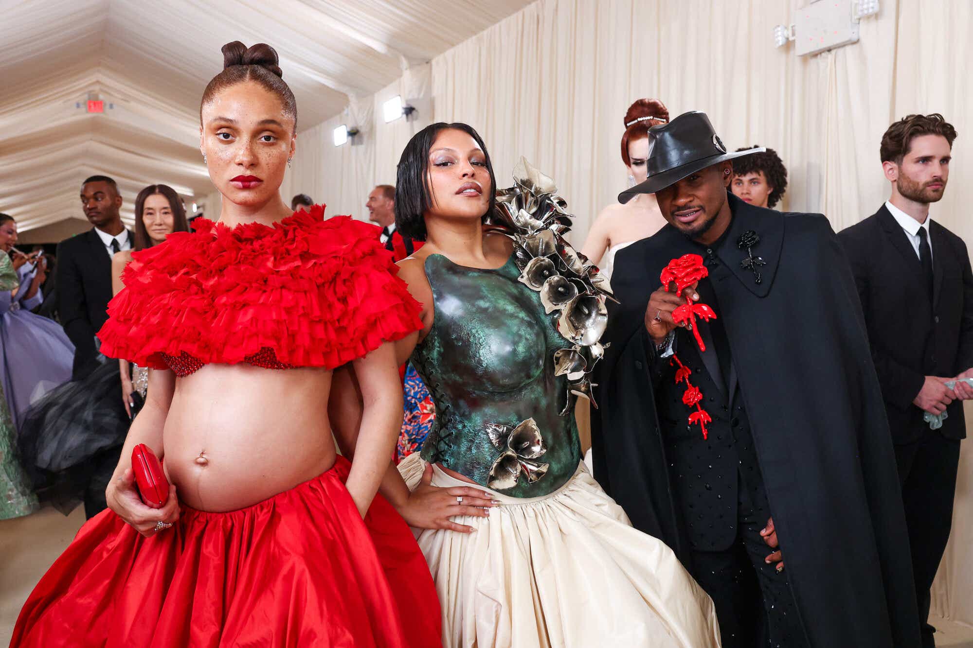 Adwoa Aboah wears a red ruffled collar over her shoulders revealing a diamante red bra underneath, with a bare belly and a wide red skirt. Paloma Elsesser wears a hard mottled green bodice adorned with large 3D metallic tulips and a wide cream skirt, and Usher wears a midnight blue suit with a cape, highwayman-cum-cowboy-style dark hat, and carries a plastic red rose.
