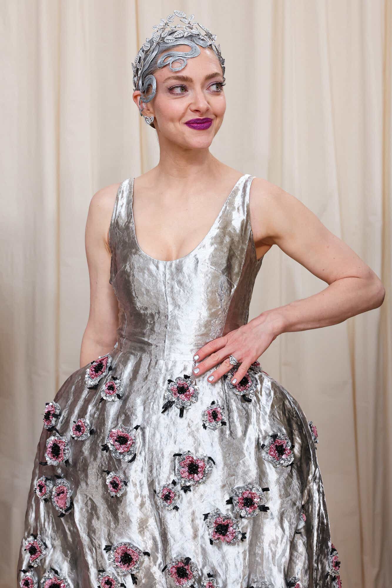 Amanda wears a sleeveless silver dress adorned with metallic silver and pink flowers and a silver imperial-style leaf headdress revealing hair sprayed into silver curls.