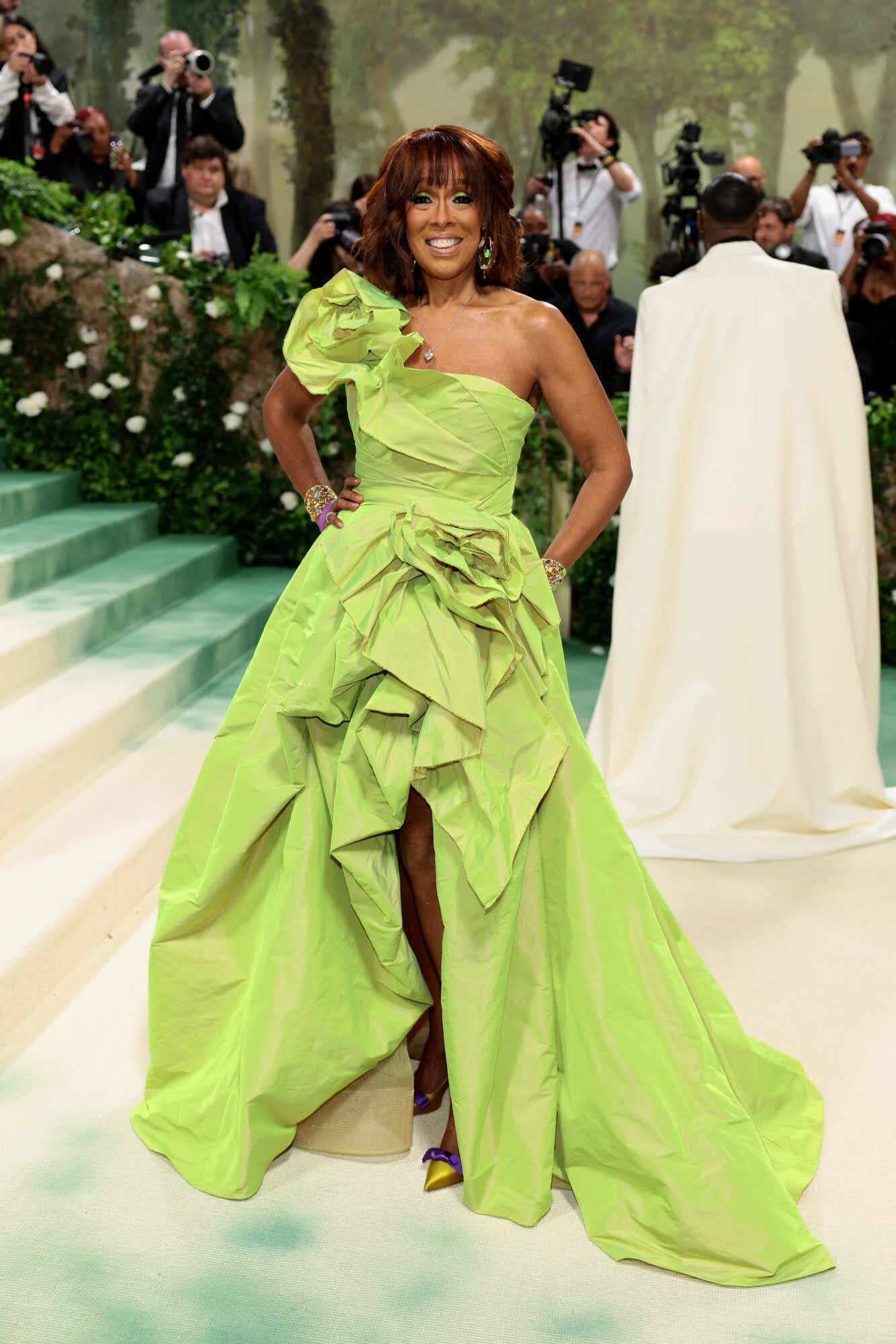 Gayle King wears a lime green one-shoulder dress with a voluminous high-low skirt and a ruffled shoulder detail.