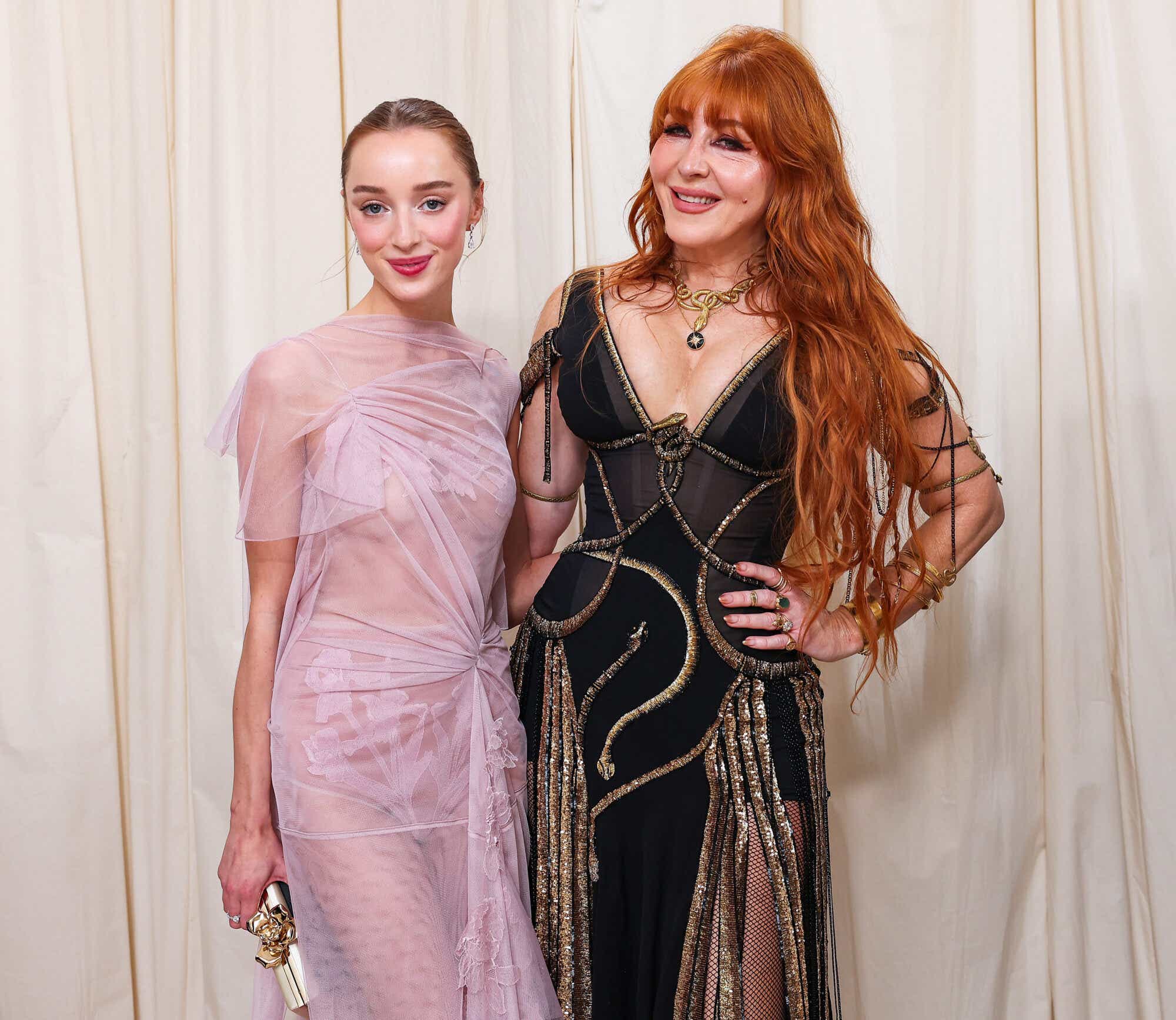 Phoebe Dynevor (R) wears a sheer pale pink tulle dress with embroidered flower detail, while Charlotte Tilbury wears a sheer corseted black dress with gold edging.