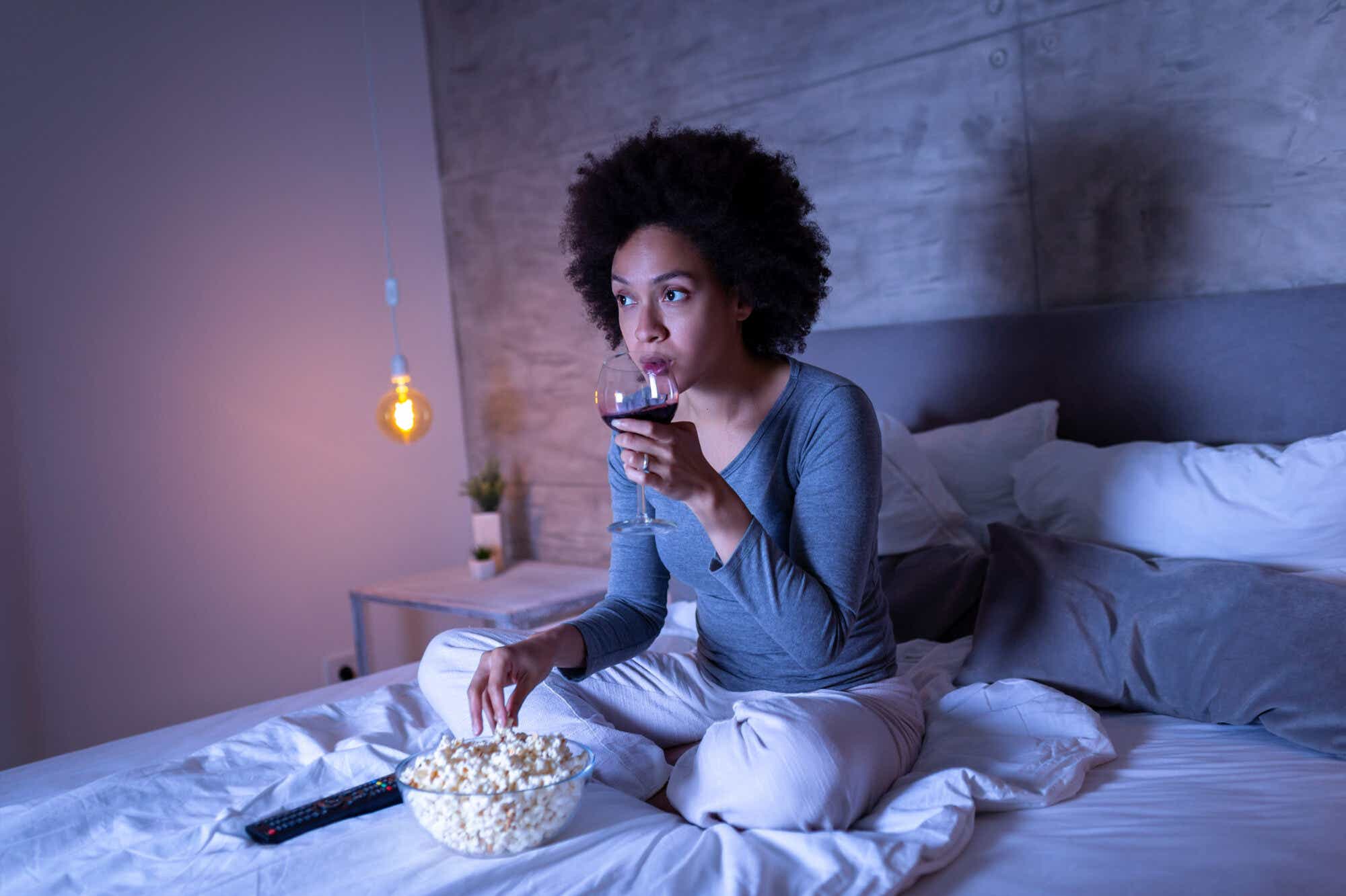 Woman eating popcorn and drinking wine in bed
