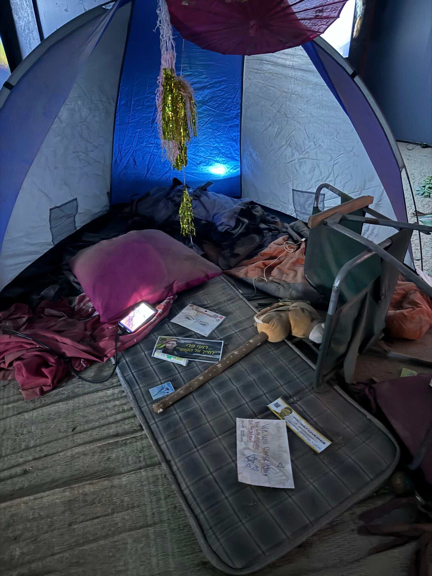 A tent filled with an overturned chair, a sleeping bag and pillow, and other items from a victim of the Nova music festival attack.