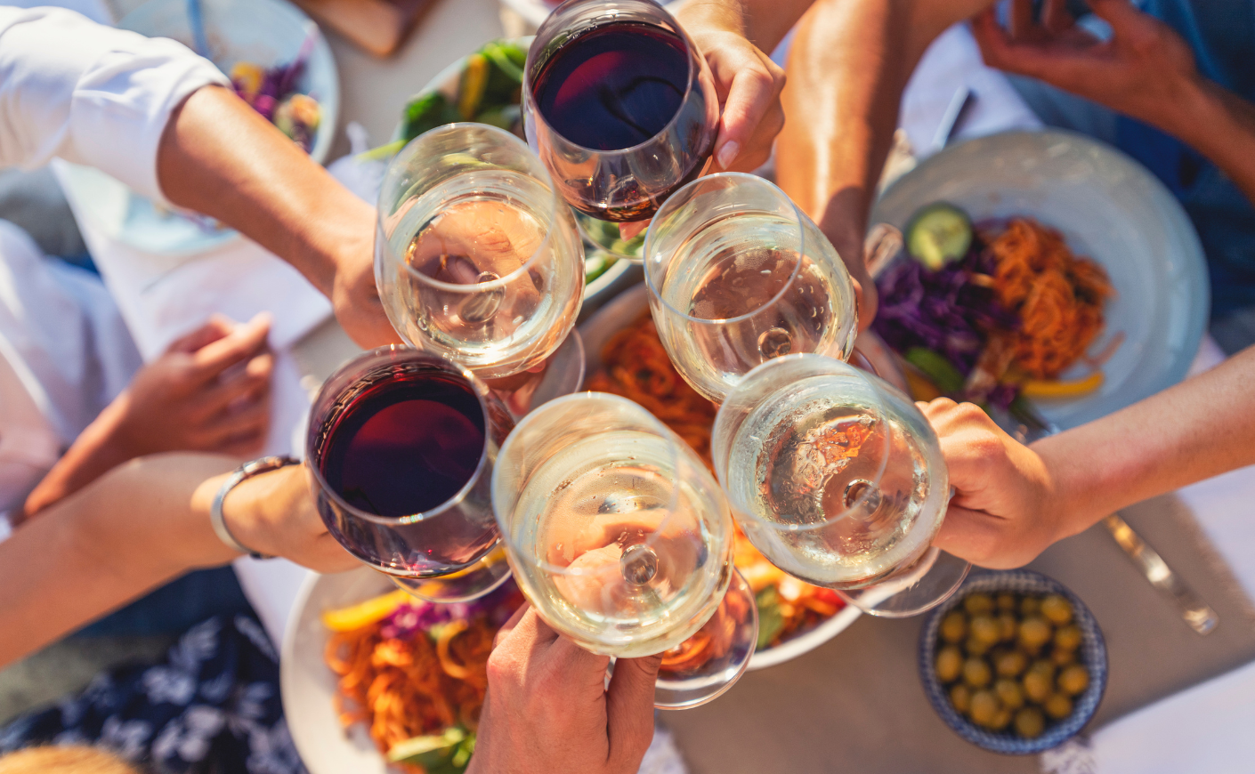 People holding glasses of wine over a table filled with food