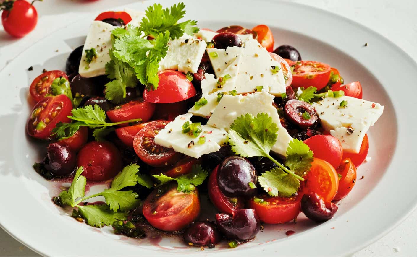 A salad with cherries, tomatoes, feta, and herbs.