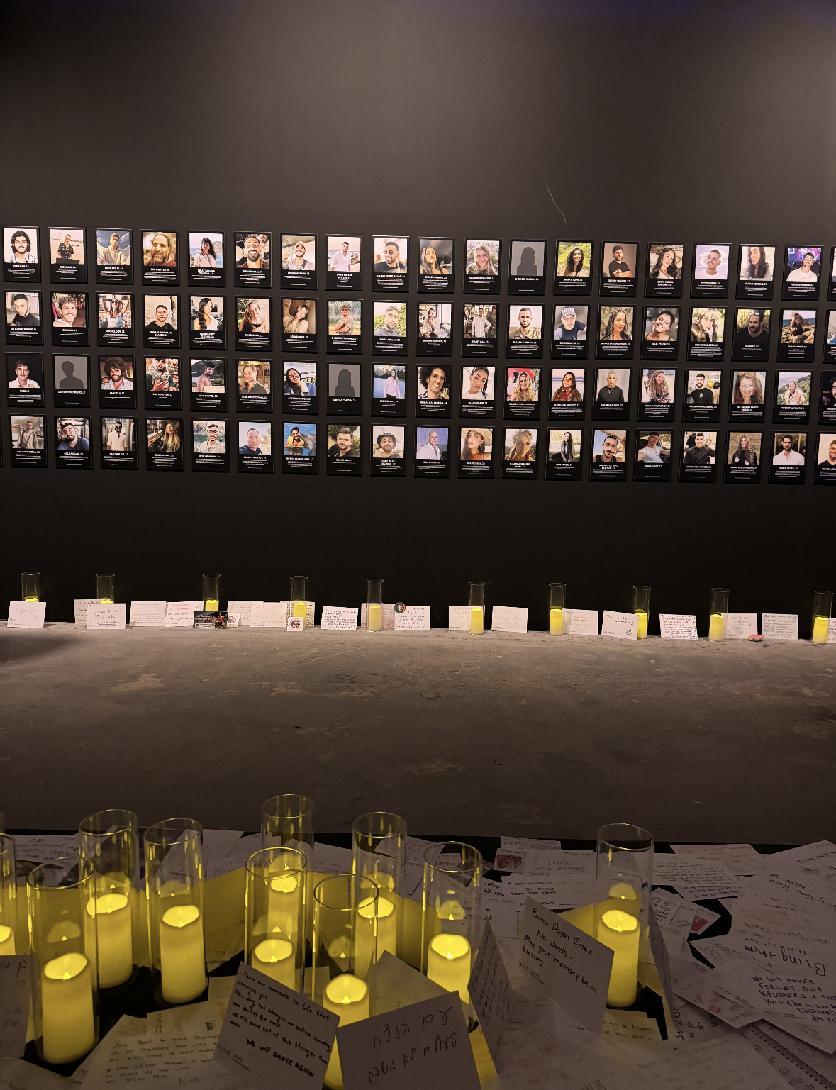 Rows of photos of the victims killed at the Nova music festival during Hamas's Oct. 7 attack. Underneath the photos are candles and letters.