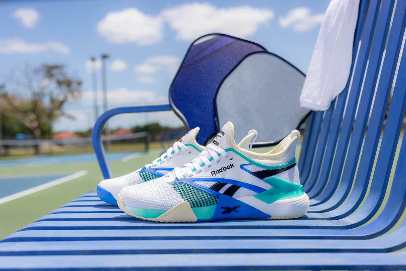 a pair of reebok pickleball sneakers on a bench on a tennis court