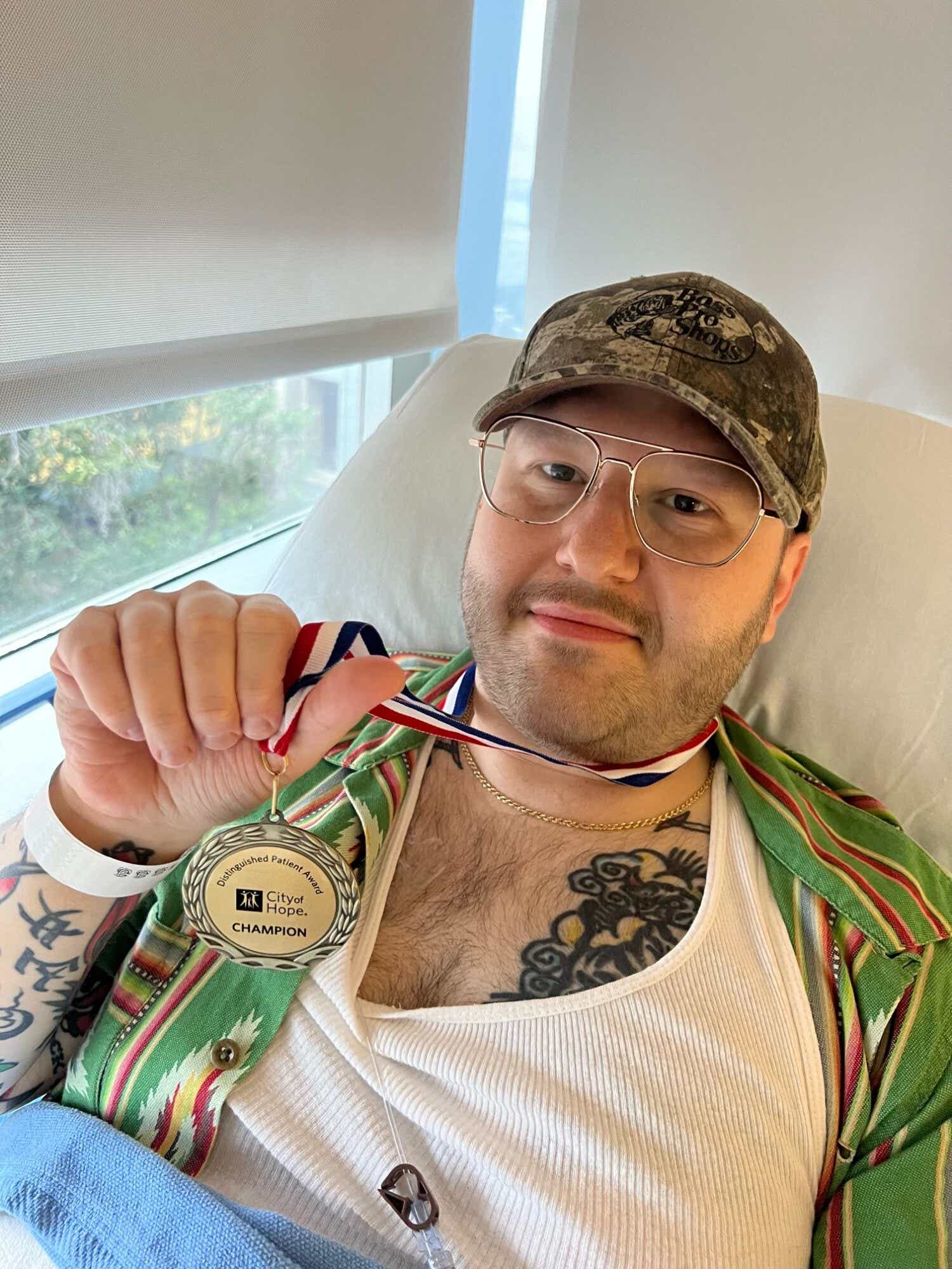 Justin Fishman lies in hospital bed and holds up medal