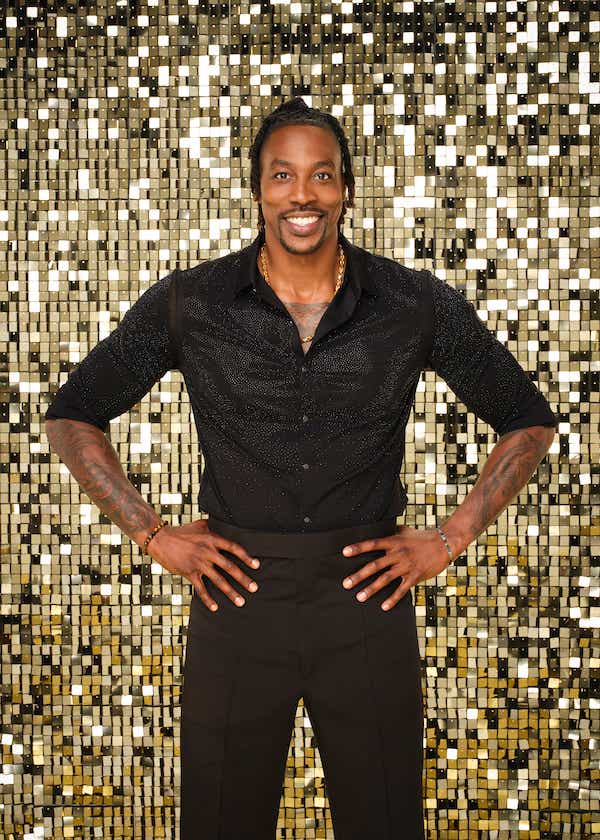 Dwight Howard wears a shimmery black button-down and poses in front of a gold wall.