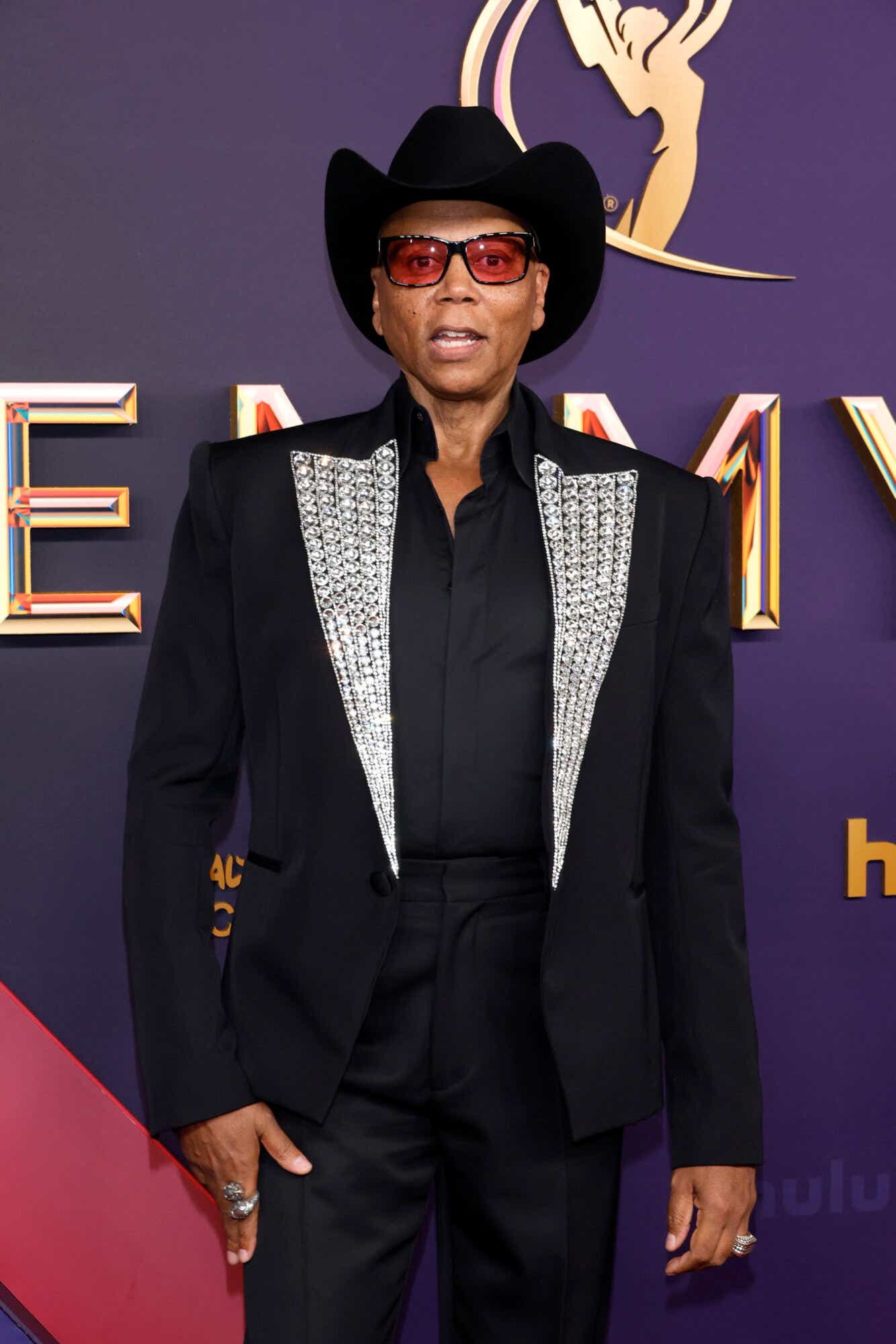 Ru Paul wears a cowboy hat, red-tinted sunglasses, and a shirt with a bedazzled lapel to the Emmys.