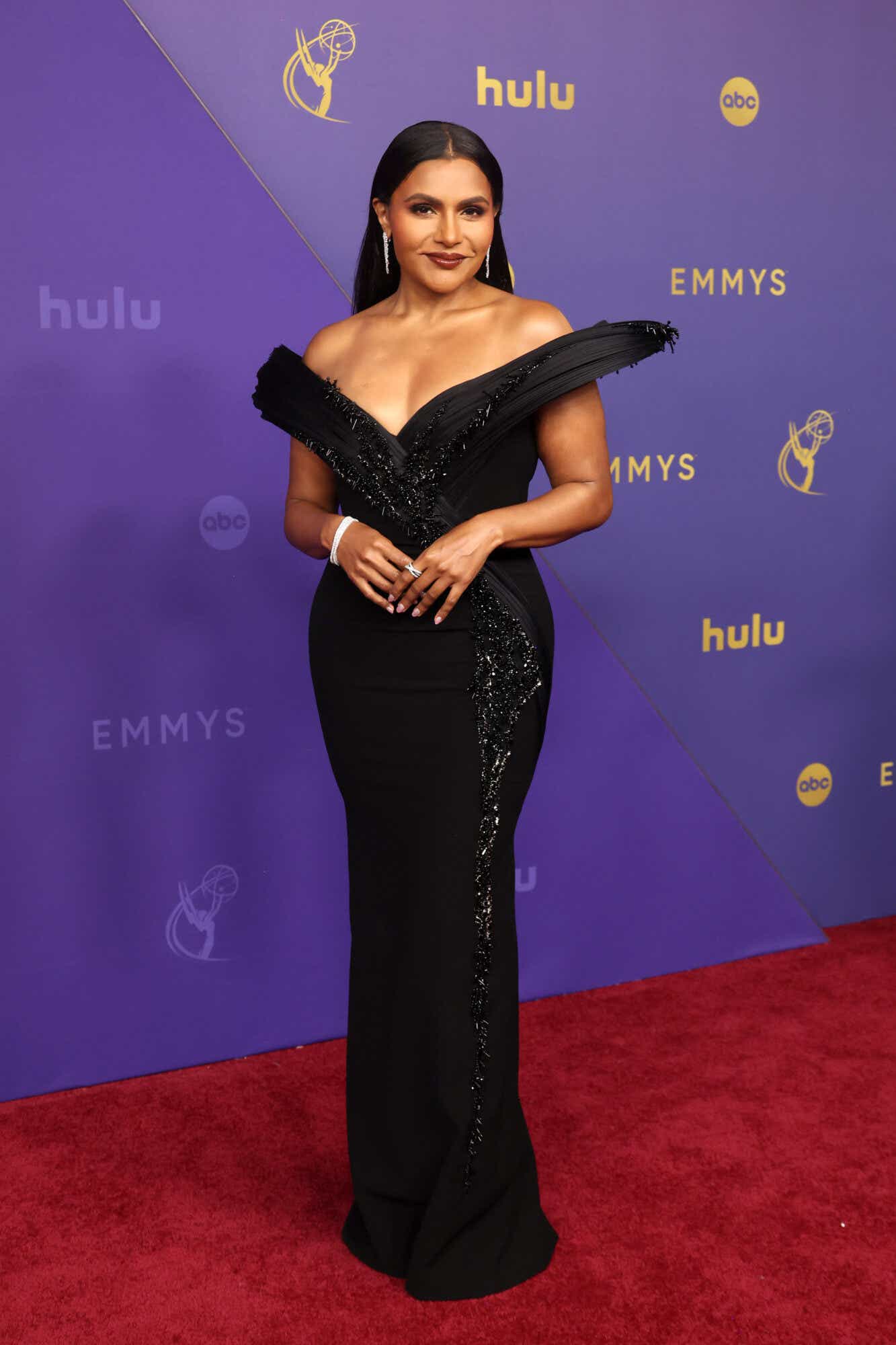 Mindy Kaling wears a black sequined gown with a dramatic off-the-shoulder silhouette.