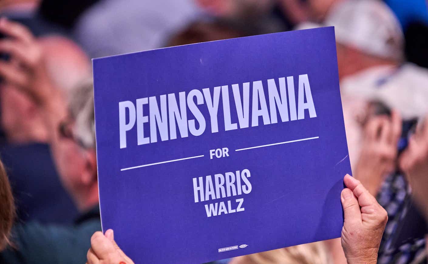 Kamala Harris supporter holding up a "Pennsylvanie for Harris/Walz sign" at a rally