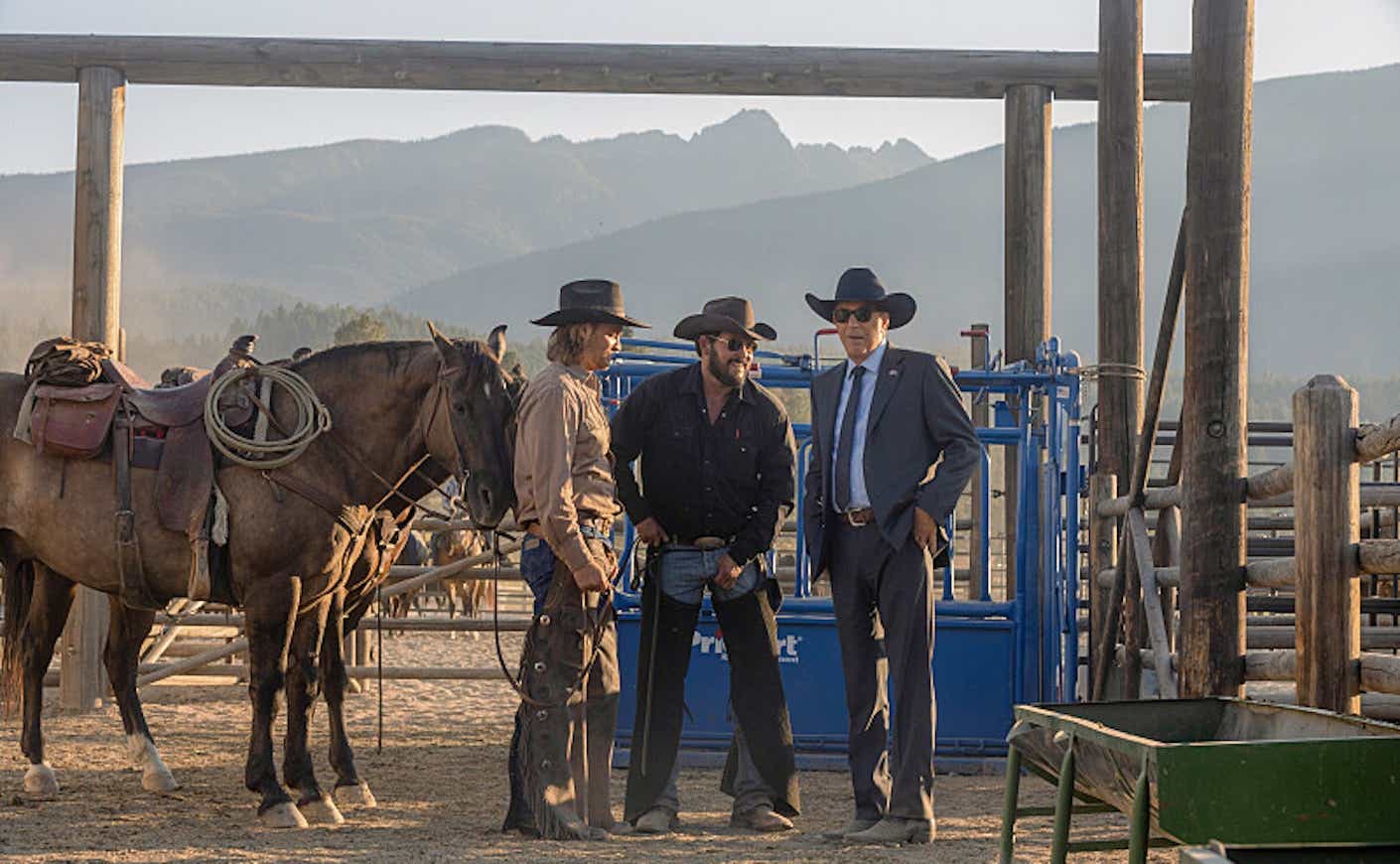 the cast of yellowstone, including kevin costner, standing on the ranch with horses