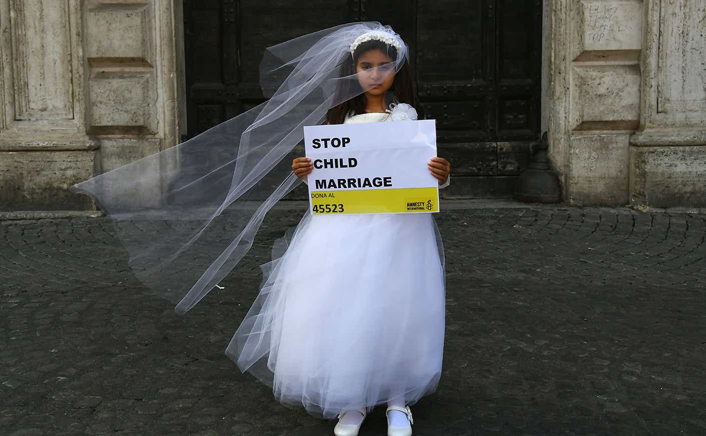 A girl in a poofy white dress and veil holding a sign that says STOP CHILD MARRIAGE