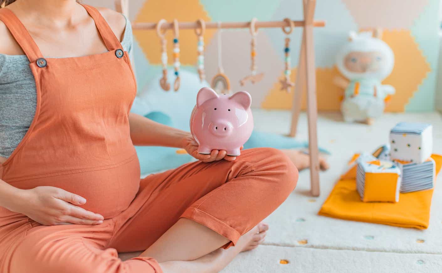 Pregnant woman holding piggy bank shopping newborn toys and nursery decor with savings.