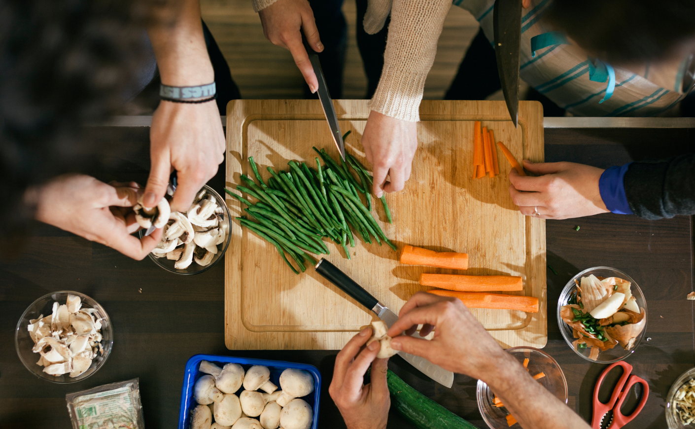 Overhead shot of multiple hands chopping food at a table