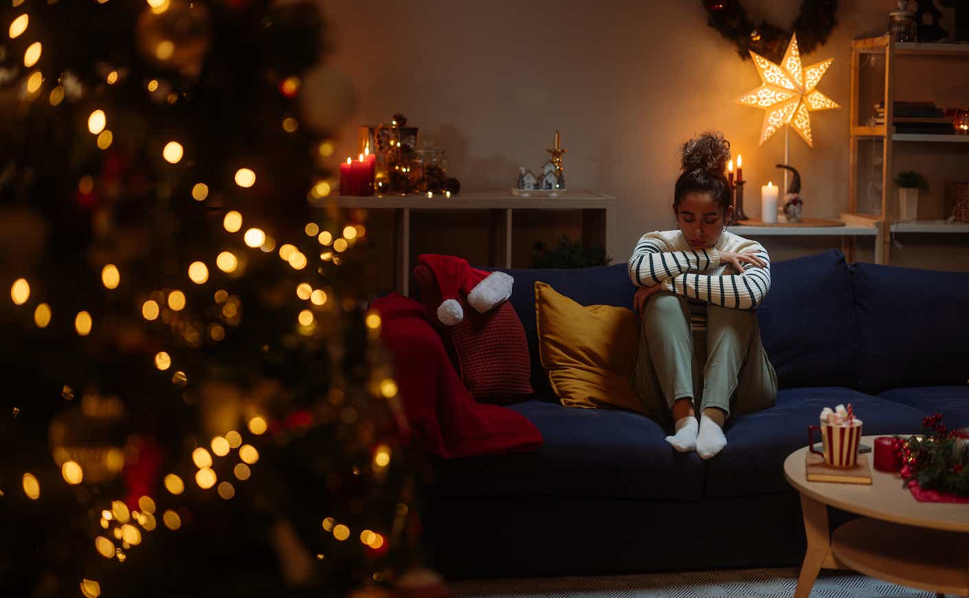 Woman looks sad sitting on couch by Christmas tree