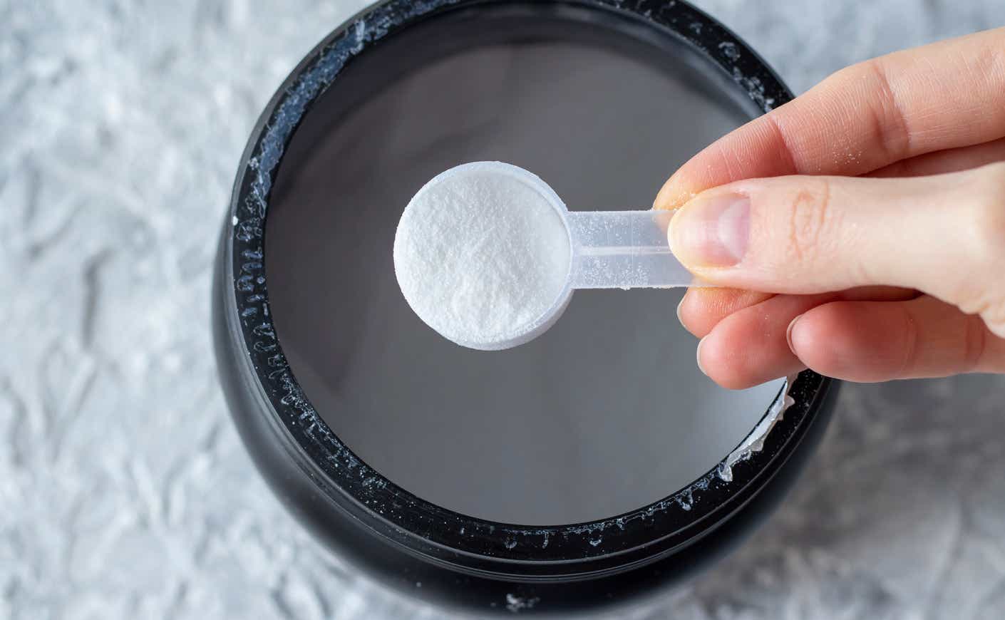 a person holding a scoop of creatine above a container