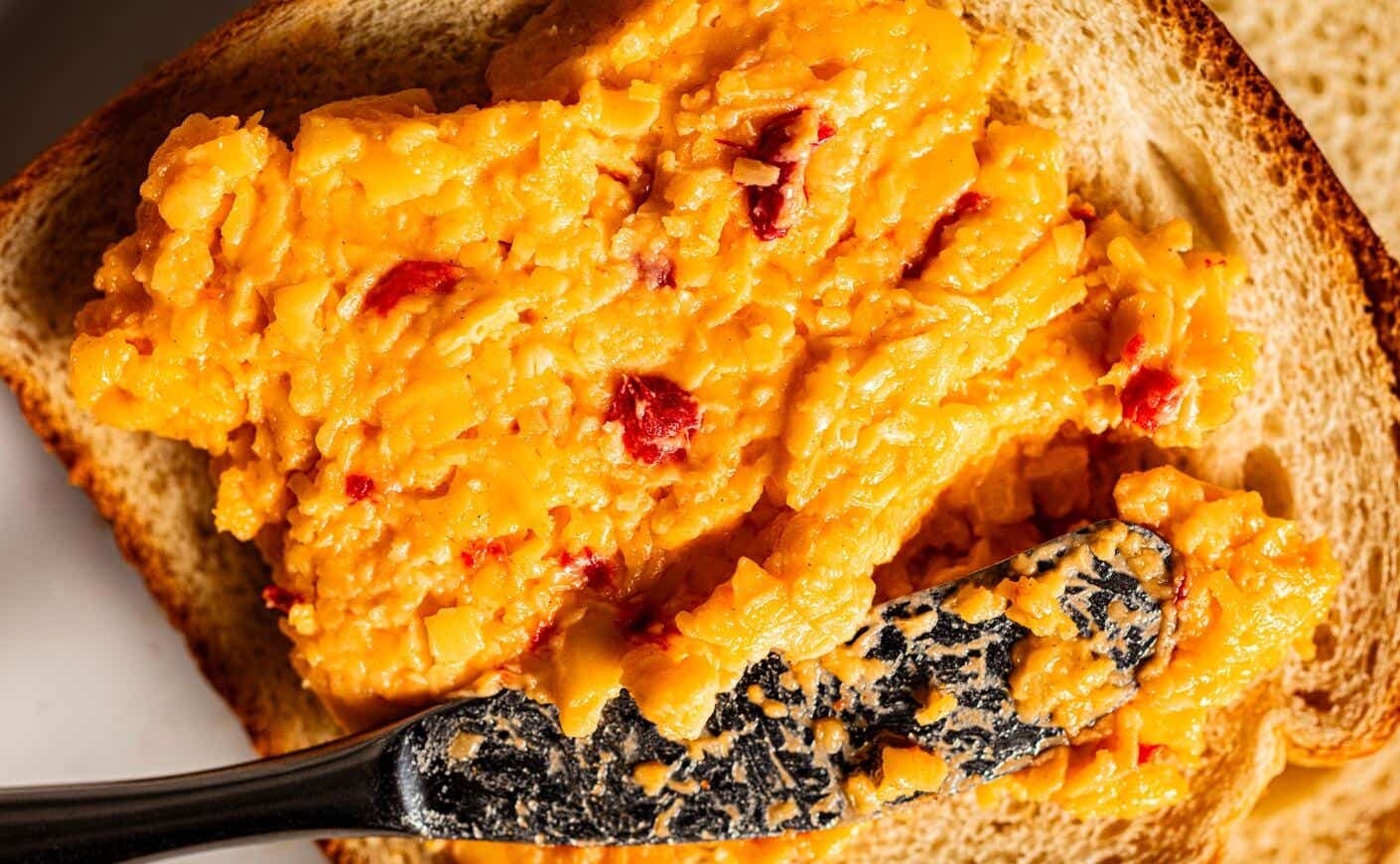 pimento cheese being spread on a slice of bread with a knife.