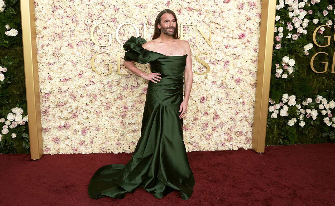 Jonathan Van Ness poses with one hand on their hip, wearing a one-shoulder olive green gown.