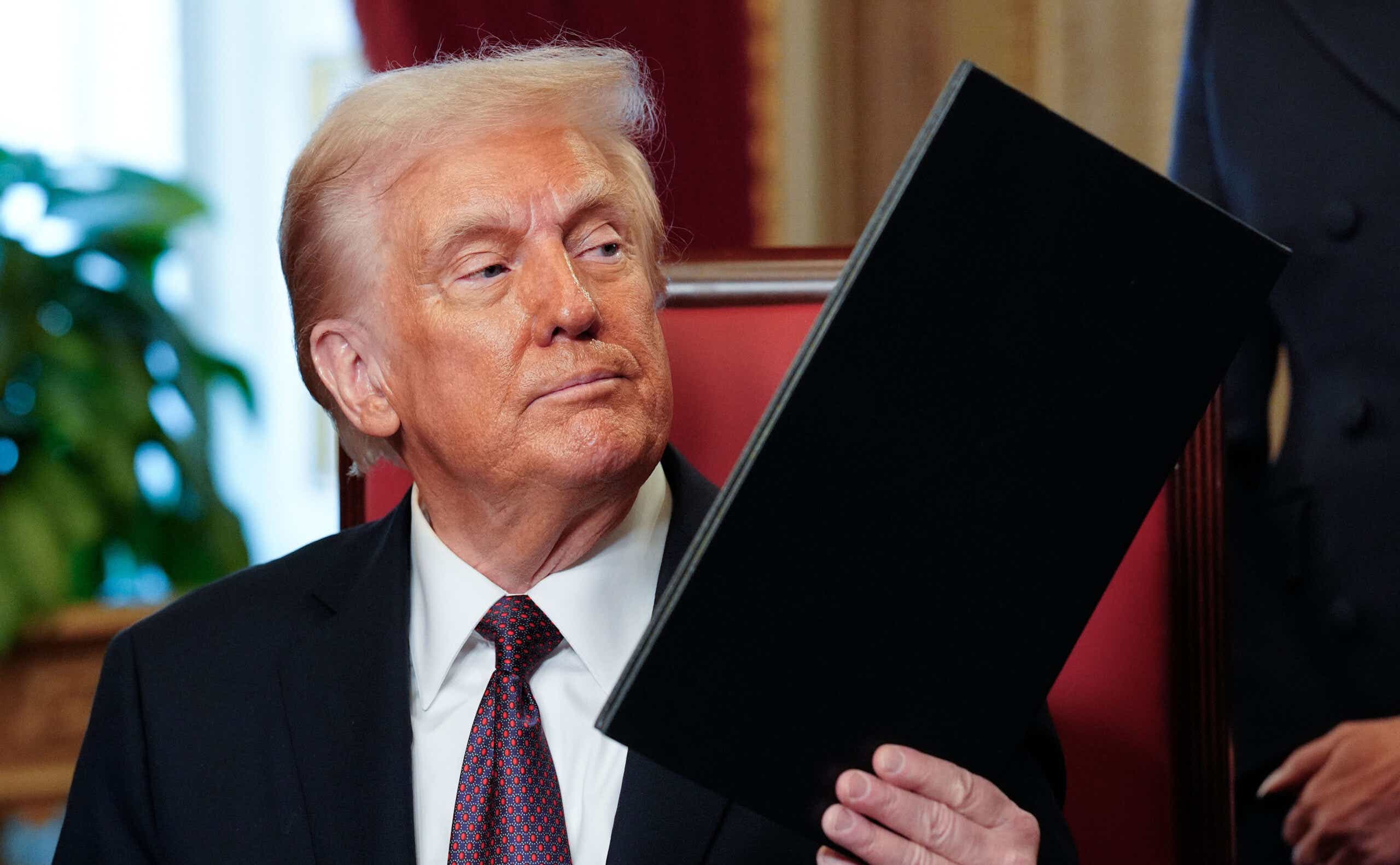 Trump sits in red chair holding black folder