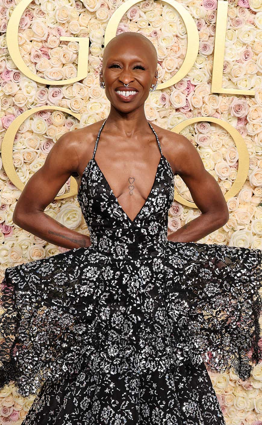 Cynthia Erivo wears a black gown with a deep V that's dotted with floral patterns made with sequins, and a dramatic peplum that flares out to the sides.