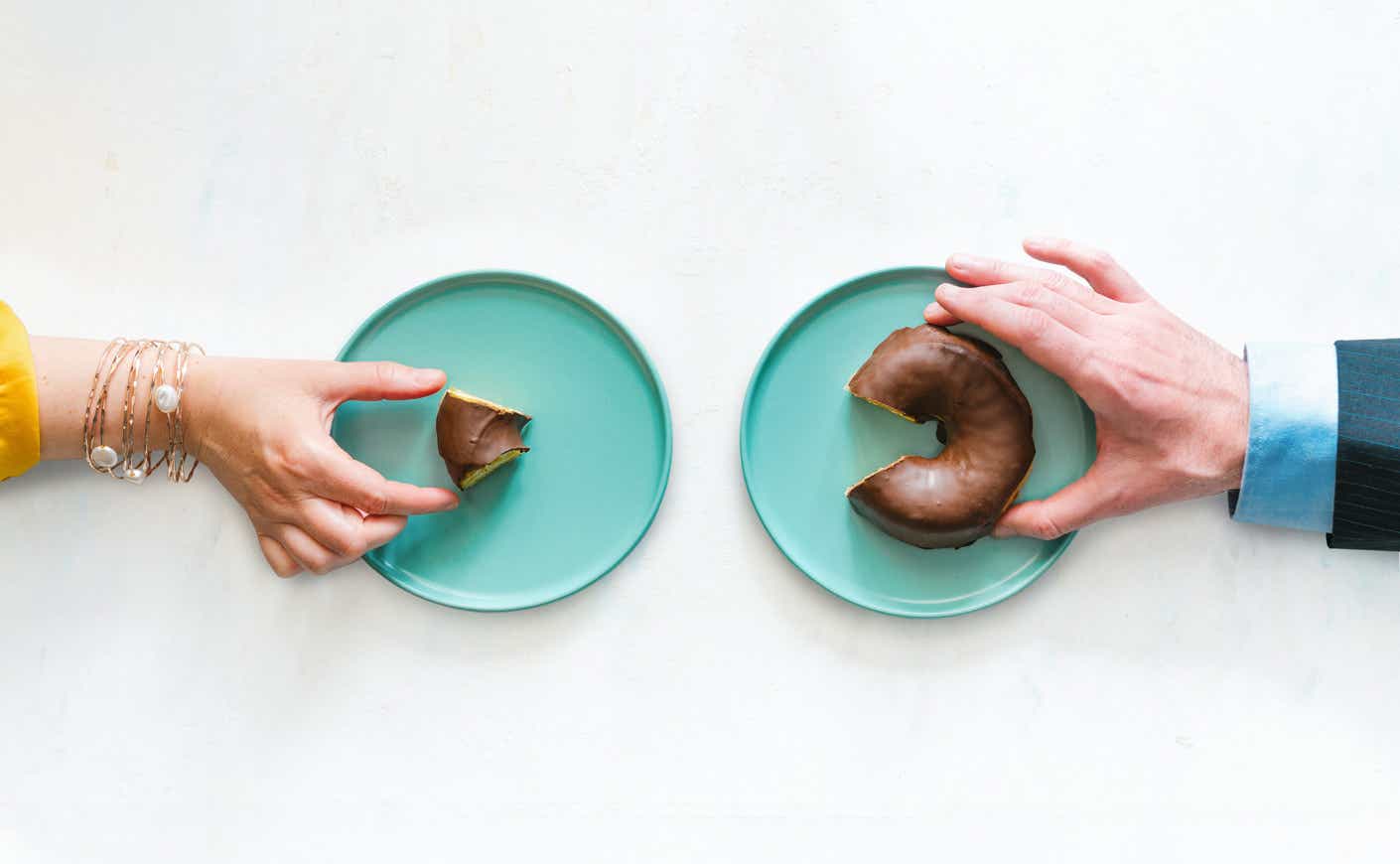 a woman reaching for a sliver of a donut and a man reaching for a larger piece