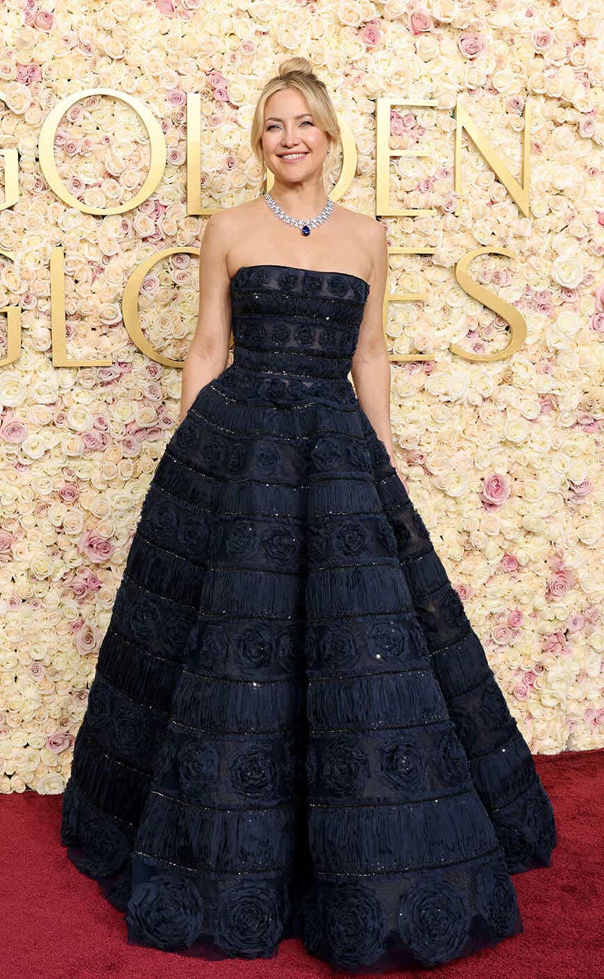 Kate Hudson wears a sparkly navy gown with a voluminous skirt and banded patterns of rosettes across the skirt and bodice.