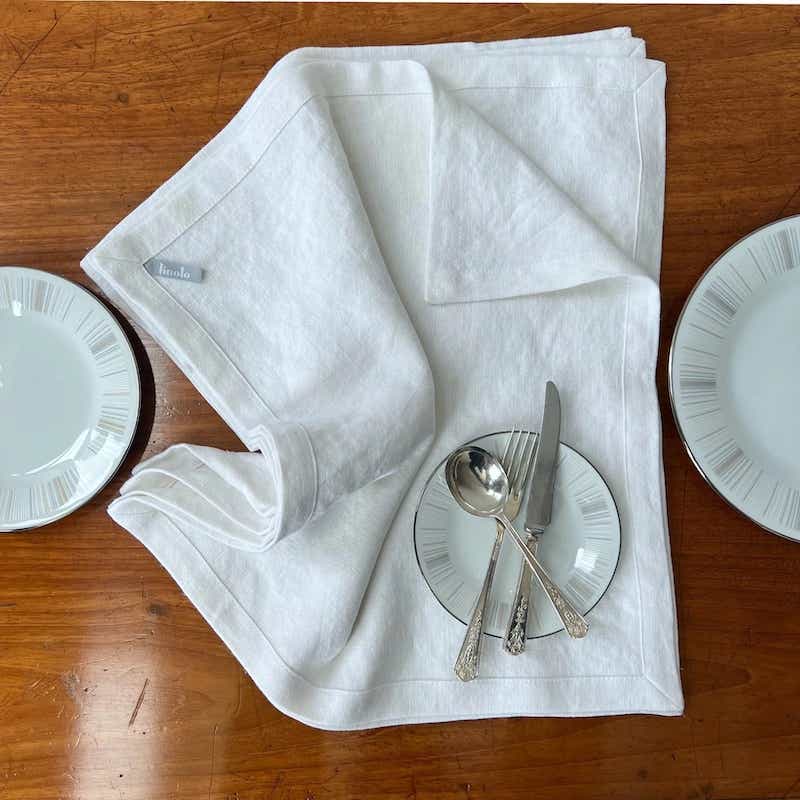 white linen napkins on a table next to plates and utensils