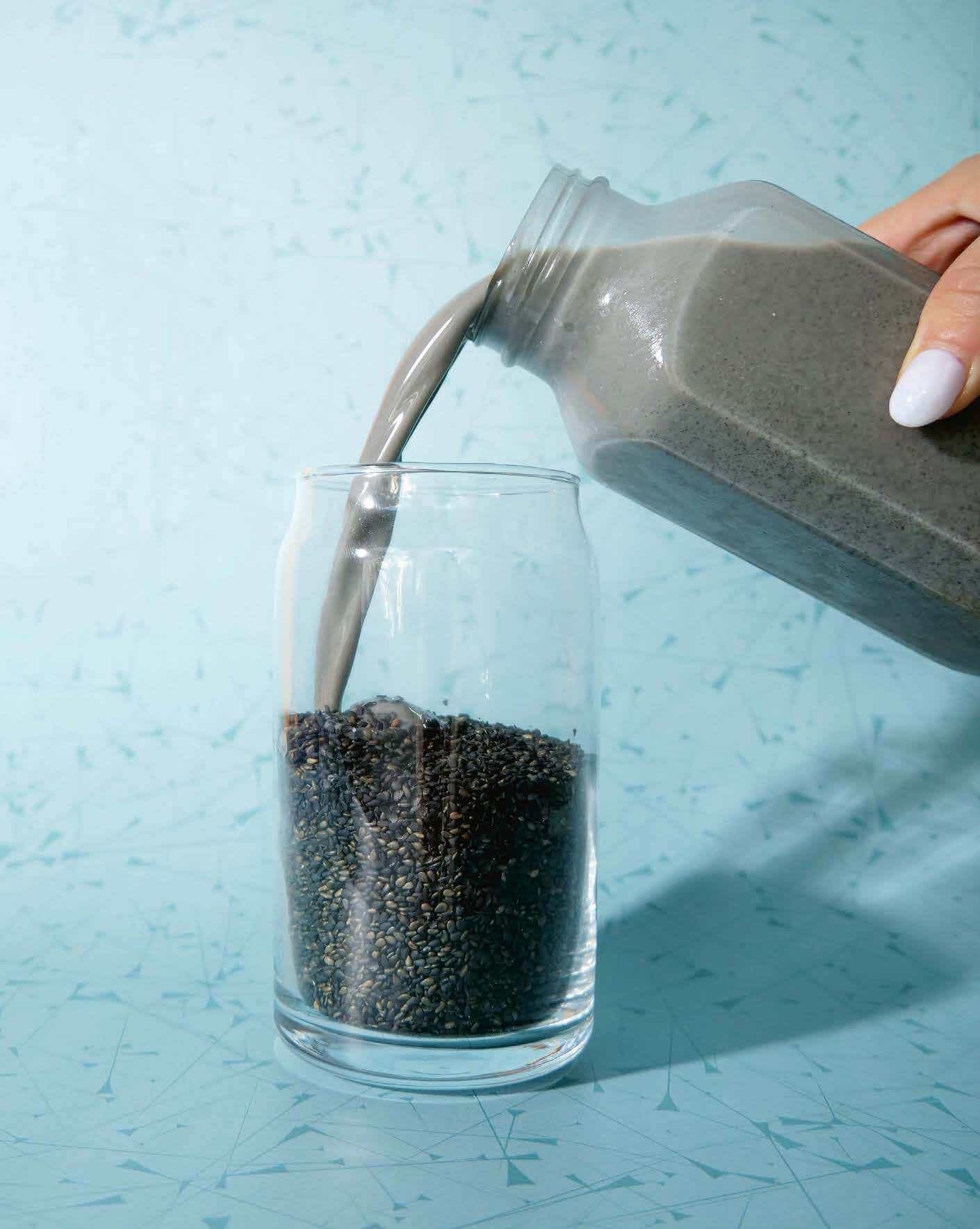 Black sesame milk being poured into a glass full of black sesame seeds.